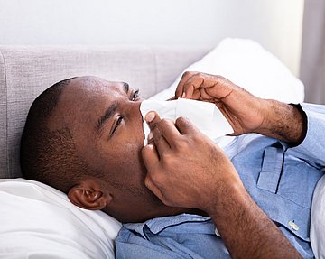 Mann im Schlafanzug liegt mit einer Sinusitis im Bett.