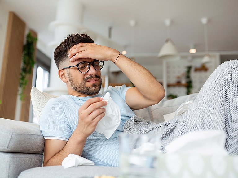 Mann liegt auf der Couch und hat Symptome einer akuten Sinusitis.