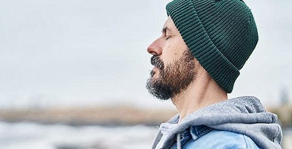 Mann im Freien stehend atmet ein.