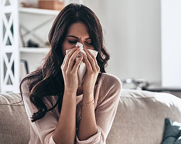 Frau mit Schnupfen schnäuzt in ein Taschentuch.