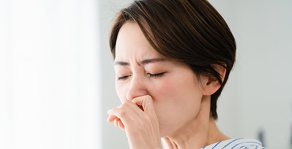 Welche Ursache führt zu einer Nasennebenhöhlenentzündung? Frau reibt sich die verschnupfte Nase.
