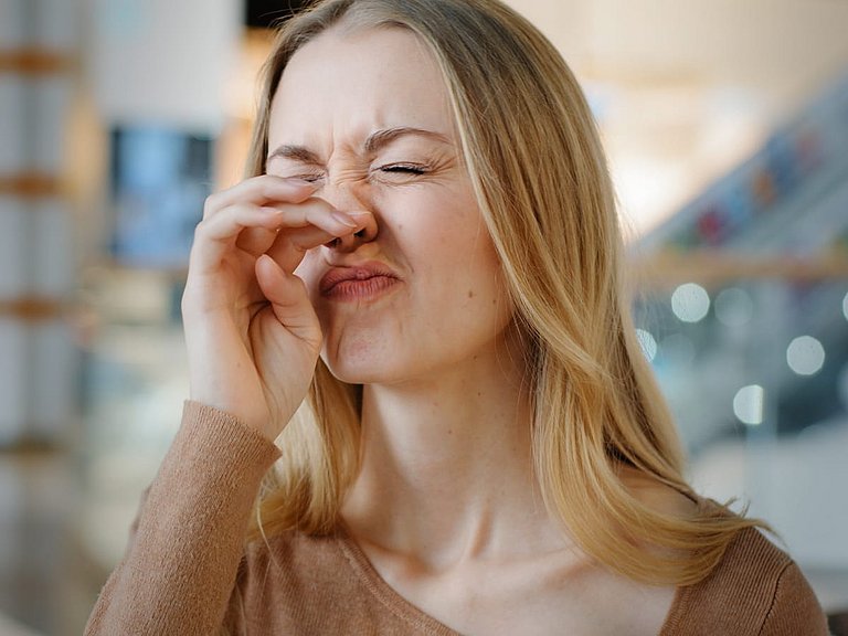 Junge Frau fasst sich mit geschlossenen Augen an die Nase. 