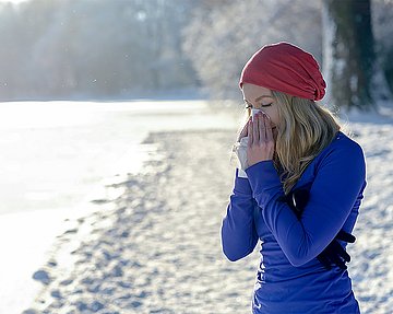 Frau mit Schnupfen macht eine Pause beim Sport im Schnee und putzt sich die Nase.