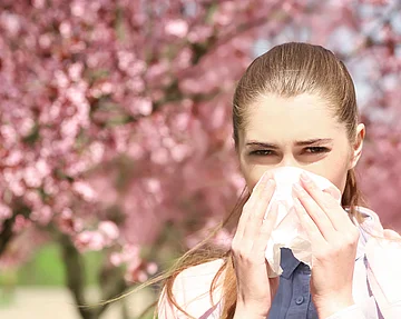Frau putzt sich vor blühenden Bäumen die Nase