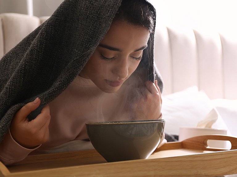 Inhalieren kann bei einer Sinusitis eine echte Wohltat sein. Frau mit einer Sinusitis beim Inhalieren mit Wasserdampf.