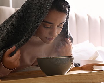 Frau mit einer Sinusitis beim Inhalieren mit Wasserdampf.